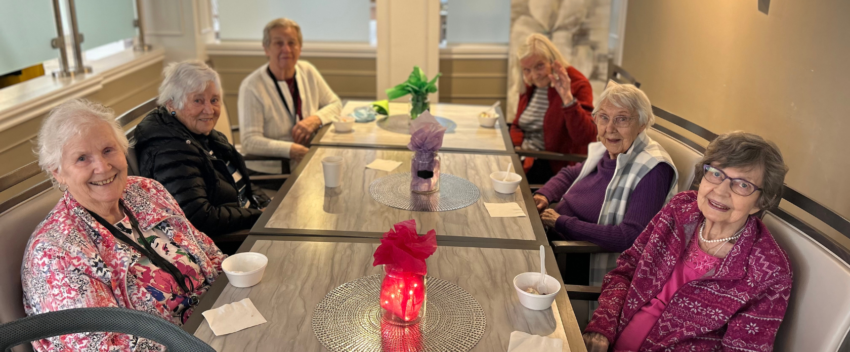 Group of women sitting at a table smiling into camera at Luther Village on the Park.